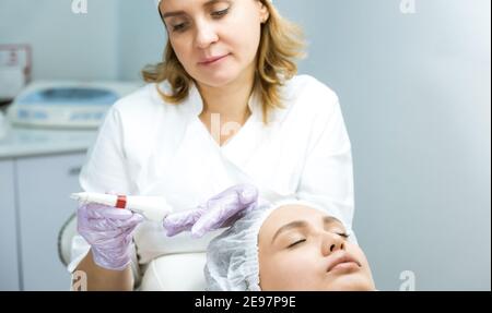Pflege und Schutz der Gesichtshaut. Eine junge Frau bei einem Kosmetikertermin. Der Spezialist trägt eine Creme-Maske auf das Gesicht Stockfoto