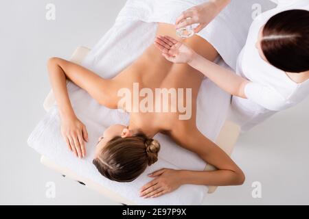 Draufsicht Masseur hält Glasflasche und gießt Massageöl In der Nähe der Frau im Spa-Salon Stockfoto
