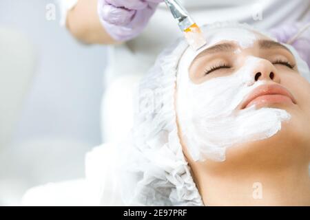 Pflege und Schutz der Gesichtshaut. Eine junge Frau bei einem Kosmetikertermin. Der Spezialist trägt eine Creme-Maske auf das Gesicht Stockfoto