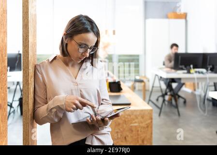 Im Stehen hispanische hübsche Frau konzentrierte sich auf ihr Tablet im Büro. Stockfoto