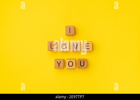 Holzwürfel mit der Phrase I Love You auf einem leeren bunten gelben Hintergrund. Worte der Liebe sind aus Briefen aus Holz für Ihre Freundin, Freund, Frau, Mann, für Valentinstag Gruß romantische Postkarte. Flach liegend, Draufsicht Stockfoto