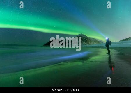 Mann am Sandstrand, der die Aurora Borealis Show mit Kopflicht beobachtet. Skagsanden Strand, Winterbedingungen, Nordnorwegen. Stockfoto