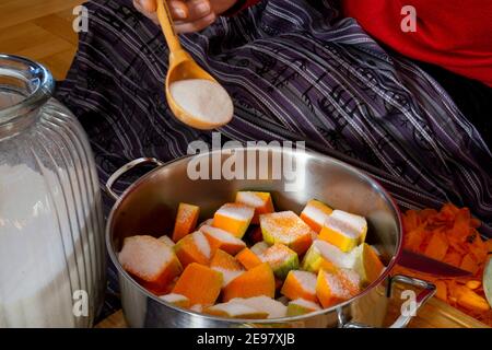 Das süße Kürbisgebäck machen. Frau schneidet und schneidet einen Kürbis auf dem Schneidebrett, während sie zu Hause auf dem Boden in der Küche sitzt. Stockfoto