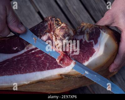 Detail von Messer schneiden spanischen Schinken auf Holztisch. Stockfoto