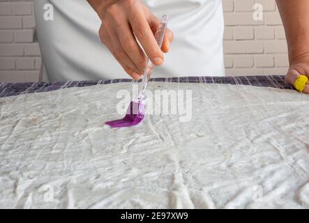 Frau und kleines Mädchen schmieren rohen Teig auf die gelegt Tisch mit einem Pinsel Stockfoto