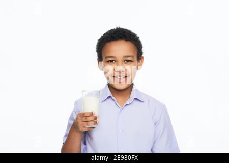 Afroamerikanische männliche Kind hält ein Glas Milch mit einem toothy Lächeln, isoliert auf weißem Hintergrund. Vorteile von Milch für Kinder Stockfoto