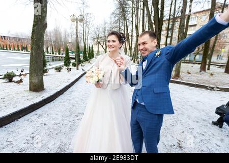 Die Braut und der Bräutigam in der Nähe des Autos, umarmen und küssen ihre Liebsten bei der Hochzeit, die Familie beim Winterfotoschießen mit der Hochzeitskortege Stockfoto