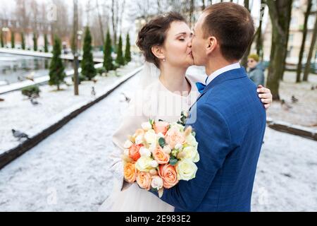 Die Braut und der Bräutigam in der Nähe des Autos, umarmen und küssen ihre Liebsten bei der Hochzeit, die Familie beim Winterfotoschießen mit der Hochzeitskortege Stockfoto