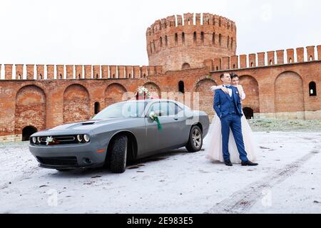 Die Braut und der Bräutigam in der Nähe des Autos, umarmen und küssen ihre Liebsten bei der Hochzeit, die Familie beim Winterfotoschießen mit der Hochzeitskortege Stockfoto