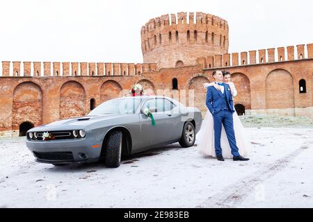 Die Braut und der Bräutigam in der Nähe des Autos, umarmen und küssen ihre Liebsten bei der Hochzeit, die Familie beim Winterfotoschießen mit der Hochzeitskortege Stockfoto
