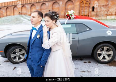 Die Braut und der Bräutigam in der Nähe des Autos, umarmen und küssen ihre Liebsten bei der Hochzeit, die Familie beim Winterfotoschießen mit der Hochzeitskortege Stockfoto