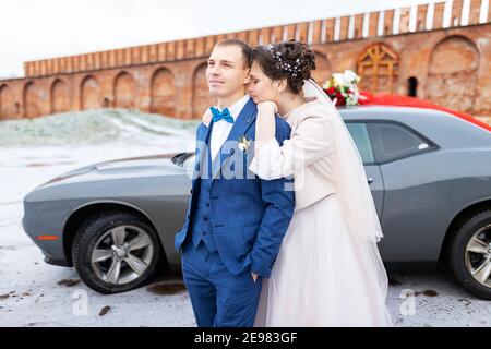 Die Braut und der Bräutigam in der Nähe des Autos, umarmen und küssen ihre Liebsten bei der Hochzeit, die Familie beim Winterfotoschießen mit der Hochzeitskortege Stockfoto