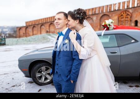 Die Braut und der Bräutigam in der Nähe des Autos, umarmen und küssen ihre Liebsten bei der Hochzeit, die Familie beim Winterfotoschießen mit der Hochzeitskortege Stockfoto