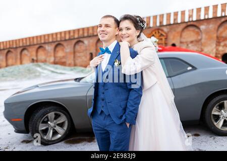 Die Braut und der Bräutigam in der Nähe des Autos, umarmen und küssen ihre Liebsten bei der Hochzeit, die Familie beim Winterfotoschießen mit der Hochzeitskortege Stockfoto
