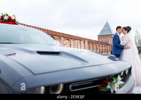 Die Braut und der Bräutigam in der Nähe des Autos, umarmen und küssen ihre Liebsten bei der Hochzeit, die Familie beim Winterfotoschießen mit der Hochzeitskortege Stockfoto
