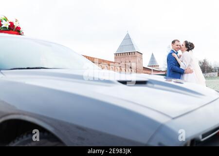 Die Braut und der Bräutigam in der Nähe des Autos, umarmen und küssen ihre Liebsten bei der Hochzeit, die Familie beim Winterfotoschießen mit der Hochzeitskortege Stockfoto
