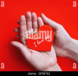 Hände halten rotes Herz vor rotem Hintergrund. Konzept Liebe, Valentinstag mit Text Ich liebe dich Stockfoto