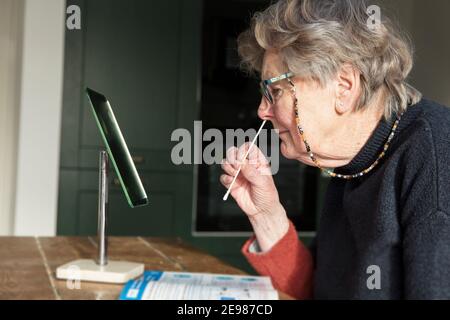 Eine Frau, die in einem Spiegel einen covid-19 nach Hause nimmt Testen des Nasenabstrichs Stockfoto