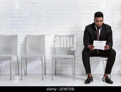 Millennial schwarz Mann liest seinen Lebenslauf während warten auf Job-Interview in Bürohalle, leeren Raum Stockfoto