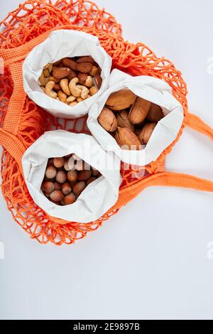Draufsicht auf verschiedene Arten von Nüssen auf dem Tisch in einer Papiertüte im Einkaufstasche Lebensmittelbeutel auf weißem Hintergrund, Zero Waste Food Shopping. Abfallfreies Wohnen, Stockfoto