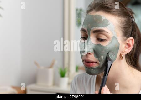 Nahaufnahme einer schönen Frauen Anwendung grünen Ton Gesichtsmaske. Bürste berührt ihre Haut. Beauty und Hautpflege Konzept. Stockfoto