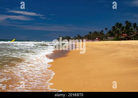 Hikkaduwa, Sri Lanka - Dezember 9. 2010: Blick auf tropischen Strand mit Palmen und Wellen von rauem Meer Stockfoto