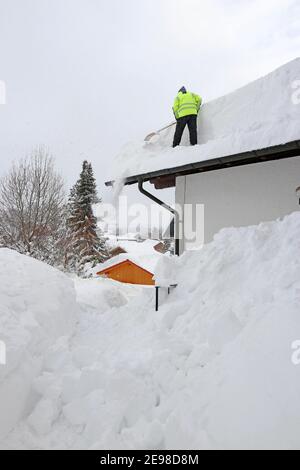 Ein Mann schaufelt hohen schweren Schnee von einem Hausdach Stockfoto