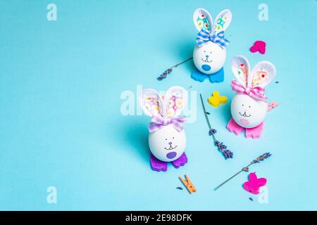 Traditionelle Ostern Symbole Konzept. Niedliche Kaninchen aus Eiern, duftende Lavendelzweige und festliche Einrichtung. Pastellblauer Hintergrund Stockfoto