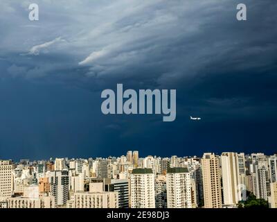 Viele Gebäude, Regenwolken und vorbeifliegendes Flugzeug. Stockfoto