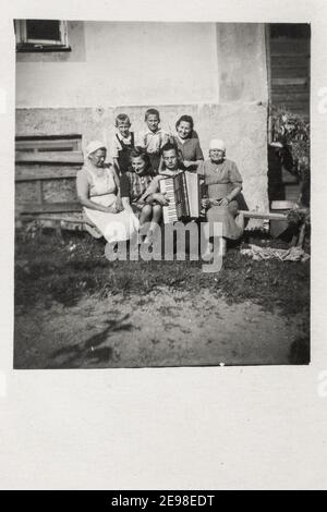 Lettland - UM 1930s: Eine Gruppe von Familien, die im Freien auf der Veranda gedreht wurde. Mann mit Akkordeons.Vintage Art Deco Ära Foto Stockfoto