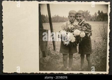 Deutschland - UM 1930s: Zwei kleine Kinder stehen und halten Blumen im Garten. Vintage Archiv Art Deco Ära Fotografie Stockfoto