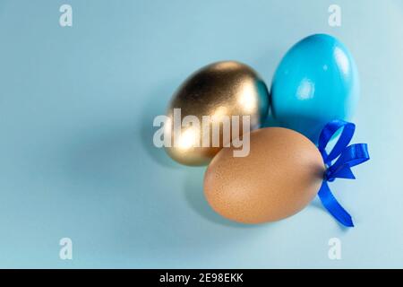 Goldene, blaue und braune Eier auf pastellblauem Hintergrund. Frohe Ostern Konzept. Baum bemalte Eier mit einem blauen Band auf einem pastellblauen Hintergrund. Kopie SPAC Stockfoto