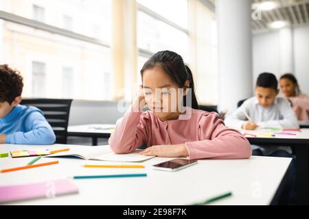 Portrait eines kleinen Mädchens, das im Klassenzimmer am Schreibtisch sitzt Stockfoto