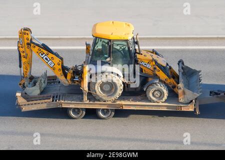 JCB 3CX Maschinen ein Traktor mit einem Eimer an der Vorder- und Rückseite zum Graben wird auf einem LKW mit Anhängerplattform auf der Autobahn transportiert. Russland, Saint-Peter Stockfoto