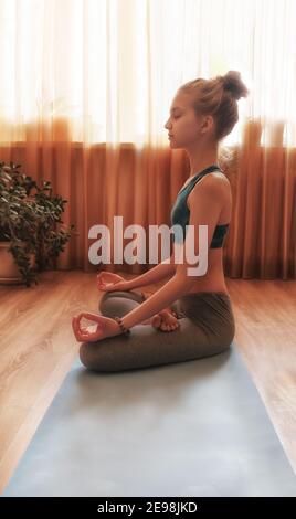 Ein schönes Mädchen, das Yoga-Übungen auf einer Yogamatte macht. Sie praktiziert früh am Morgen zu Hause.Meditation Stockfoto