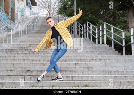 Hübscher junger Mann, der Make-up trägt und Ballett auf Treppen tanzt. Nicht binäre androgyne Kerl. Stockfoto