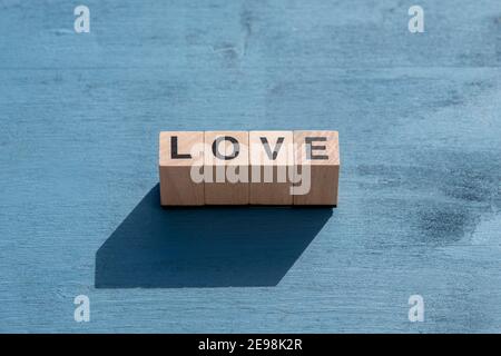 Valentinstag und Happy Emotion Konzept: Das Wort LIEBE mit einzelnen Holzwürfelbuchstaben für Brettspiele auf blauer Strukturfläche geschrieben. Stockfoto