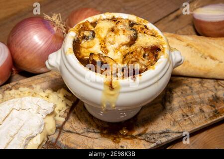 Eine köstliche Schüssel mit französischer Zwiebelsuppe mit Camembert und einer Cheddar-Kruste, umgeben mit den Zutaten, die verwendet werden, um das Gericht als Holzküche zu erstellen Stockfoto
