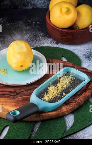Zitronenschale und Reibe auf einem Holzbrett auf schwarzem Hintergrund. Selektiver Fokus. Stockfoto
