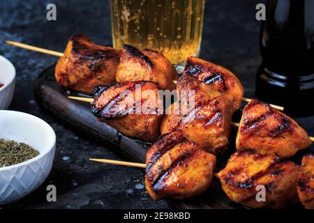 Einfach und lecker Chicken Kebabs. Gegrilltes Hähnchen auf Bambusspießen mit einem Getränk. Dunkler Hintergrund. Stockfoto