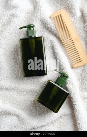 Grüne Spender Flaschen Shampoo und Duschgel, Holzkamm auf weißem Handtuch im Badezimmer. SPA natürliche Bio-Kosmetik-Set, Haarpflege-Konzept. Stockfoto