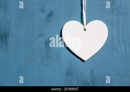 Liebe und Grüße Konzept: Draufsicht auf ein einziges weißes leeres Herz, das über einem hölzernen blauen Hintergrund mit Kopierraum hängt. Feier für Freunde Stockfoto