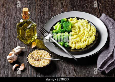 Brokkoli Kartoffelpüree mit gehackten Mandeln bestreut serviert mit gedünsteten Brokkoli blüsst auf einem schwarzen Teller auf einem dunklen Holz Tabelle Stockfoto