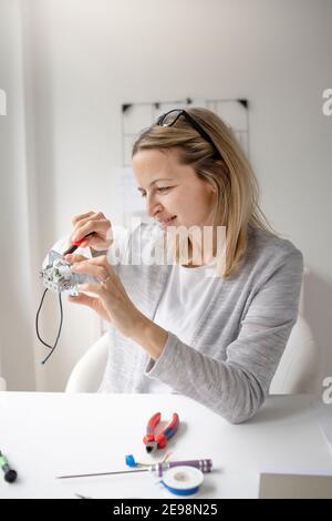 Schöne, blonde Elektrikerin sitzt am Tisch im Büro Befestigung einer Steckdose Stockfoto