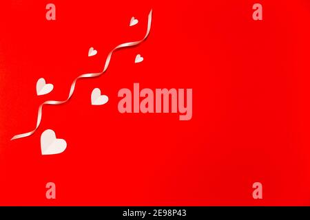 Weiße Papierherzen mit weißem Farbband über dem roten Hintergrund in flacher Lay-Optik. Komposition zum Valentinstag. Urlaubskonzept. Stockfoto