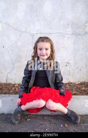 Süßes Mädchen trägt ein rotes Tutu sitzt vor einer Betonwand. Stockfoto