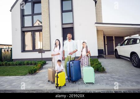 Foto-Porträt von lächelndem Paar Frau Mann mit kleinen Kindern Koffer vor dem Haus für die Reise bereit halten Stockfoto