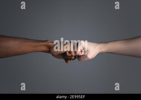Nahaufnahme des weißen und des dunkelhäutigen Mannes, der eine Faust-Beule auf grauem Hintergrund mit Kopierraum isoliert macht. Stockfoto
