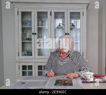 Eine Frau hat morgens ein Queo Kaffee, während sie das Papier liest und ein Kreuzworträtsel vervollständigt. Stockfoto