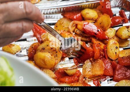 Gegrillte Kartoffeln und Tomaten auf Aluminiumfolie Tablett direkt vom Grill serviert, Nahaufnahme Detail auf Silbergabel in Gemüse Stockfoto